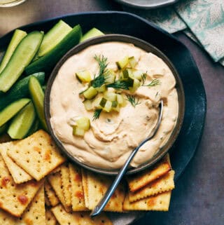 overhead view of a bowl of dill pickle dip surrounded by crackers and cut vegetables