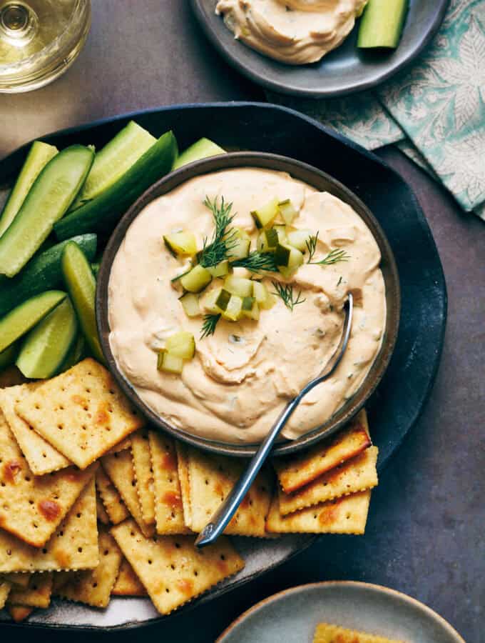 overhead view of a bowl of dill pickle dip surrounded by crackers and cut vegetables