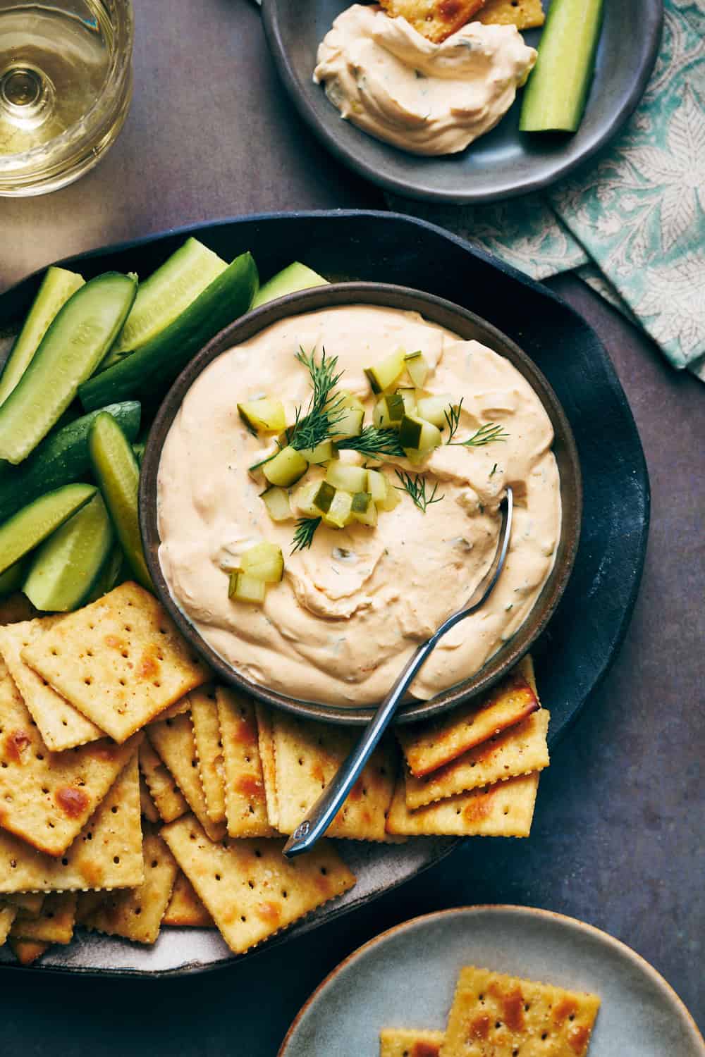 overhead view of a bowl of spicy dill pickle dip with saltine crackers and cucumber on the side