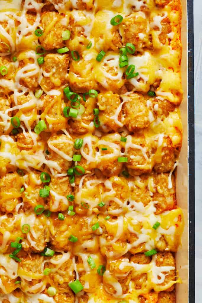 closeup of baked casserole with tater tots and extra cheese melted on top and scallions