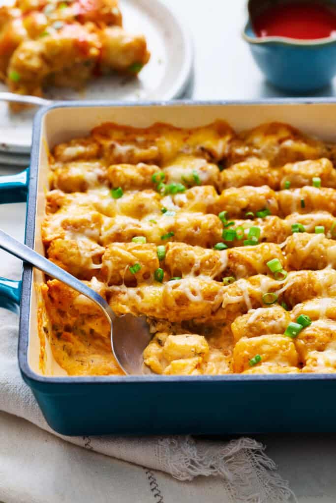 scooping buffalo chicken tater tot casserole out of a dish