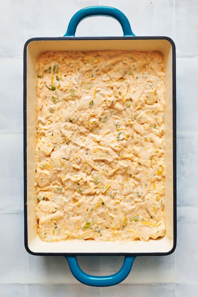 a layer of buffalo chicken in a creamy sauce in the bottom of a green 9 x 13 pan