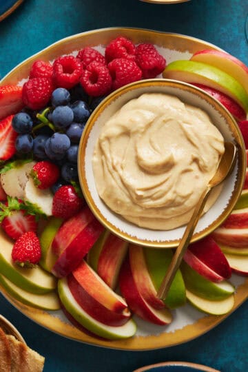 overhead view of a fruit platter with cheesecake fruit dip surrounded by apples, berries and grapes