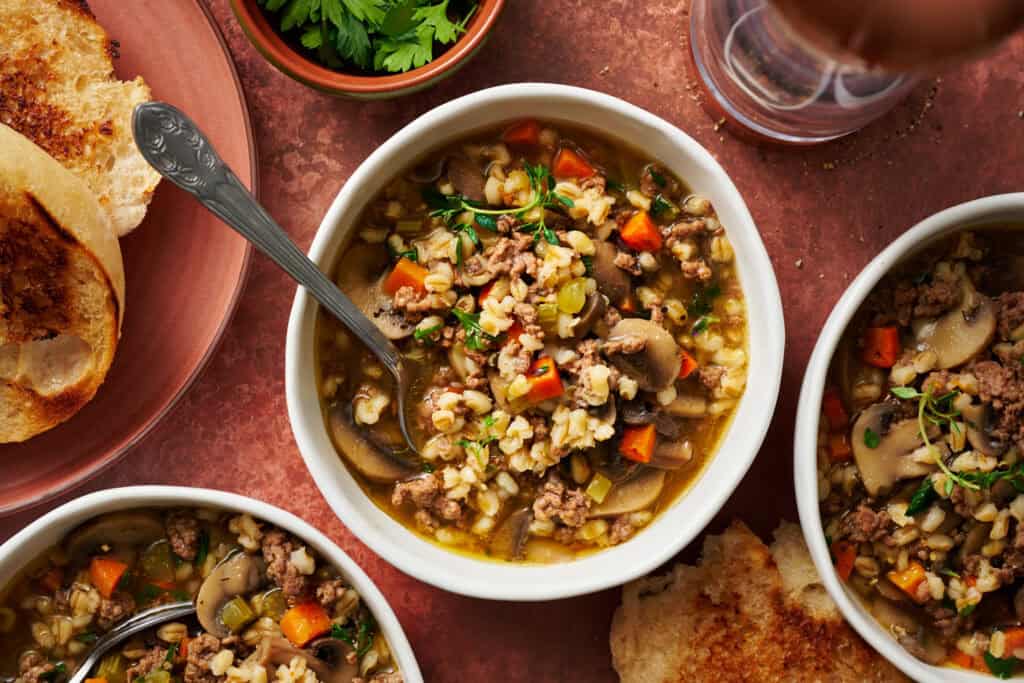 overhead view of a bowl of pressure cooker beef barley soup with bread on the side