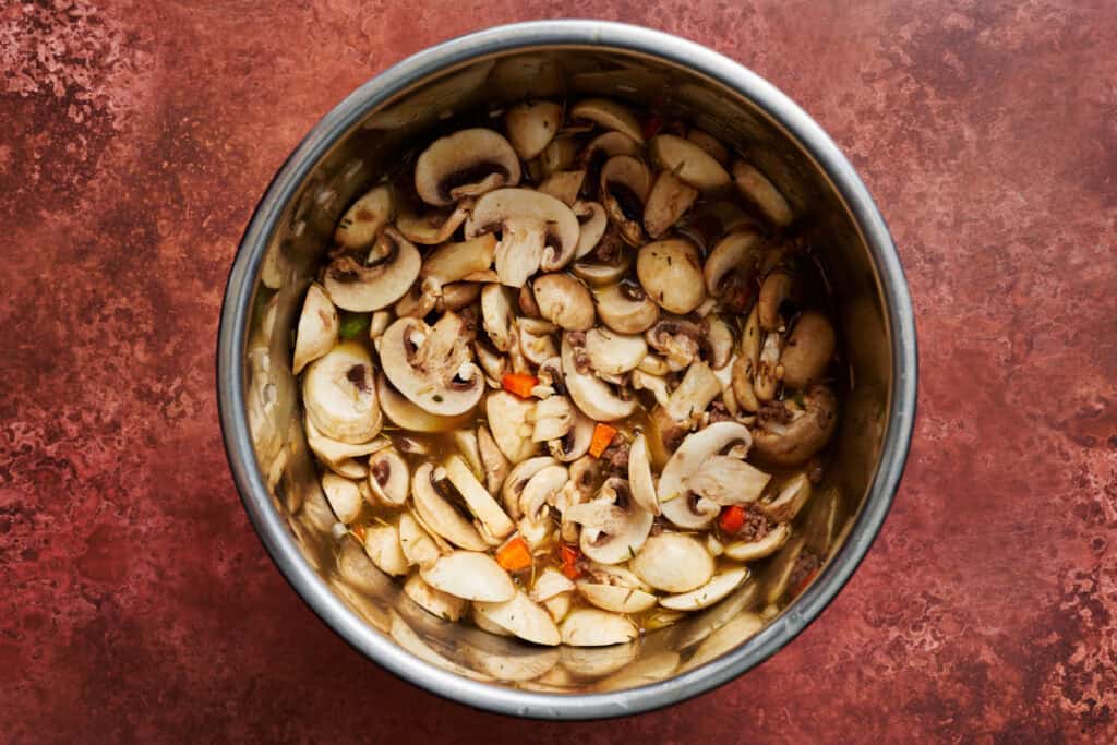 all the ingredients for the soup including mushrooms and broth added to the Instant Pot