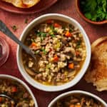 overhead view of a bowl of pressure cooker ground beef barley soup with a spoon and parsley on the side