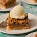 Bourbon pecan pie bar on a plate topped with ice cream and a fork on the side.