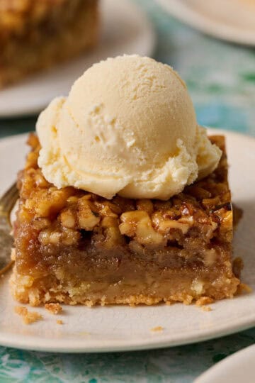 Bourbon pecan pie bar on a plate topped with ice cream and a fork on the side.