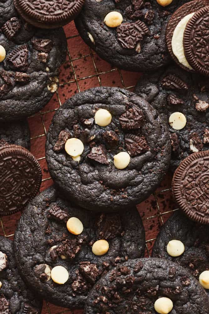 Baked Chocolate Cookies and Cream Cookies layered on a cooling rack surrounded by extra Oreo cookies.