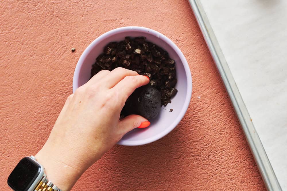 pressing cookie dough ball into chopped oreo cookies