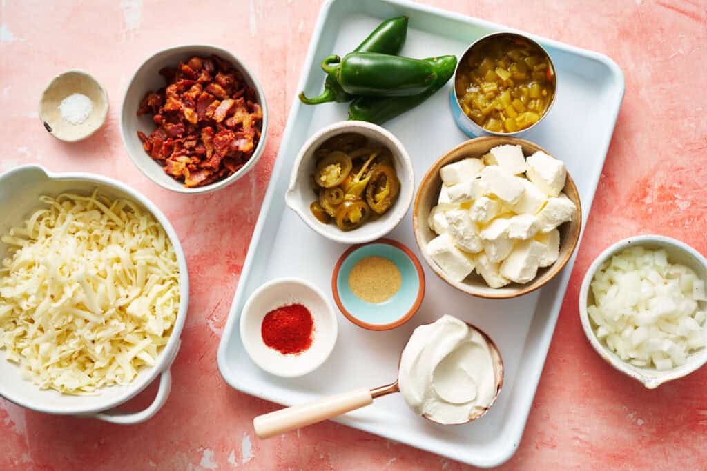 ingredients for crock pot jalapeno popper dip including onions, sour cream, paprika, garlic powder, cream cheese, cheese, jalapenos, diced green chilis, bacon and salt