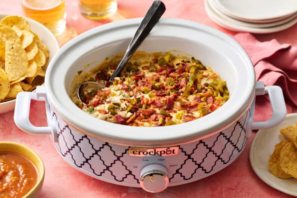 crock pot jalapeno popper dip with pickled jalapenos and bacon crumbled on top with chips and beer on the side