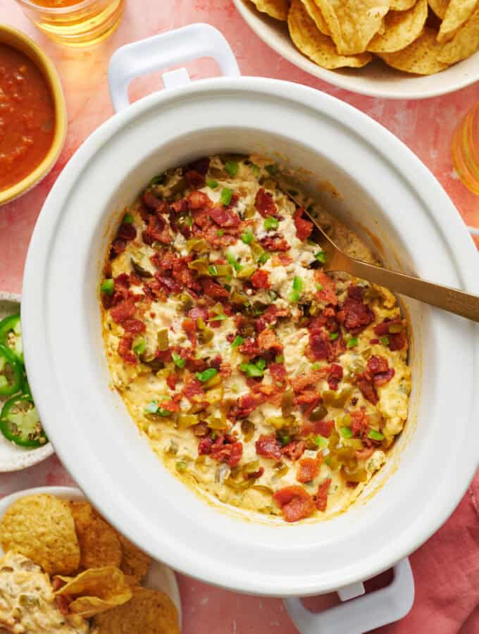 overhead view of a slow cooker with jalapeno popper dip ready to serve with chips and salsa on the side