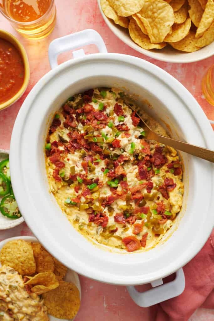 overhead view of a slow cooker with jalapeno popper dip ready to serve with chips and salsa on the side