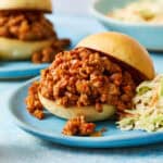 A ground chicken sloppy joes sandwich on a blue plate with another sandwich int he background.