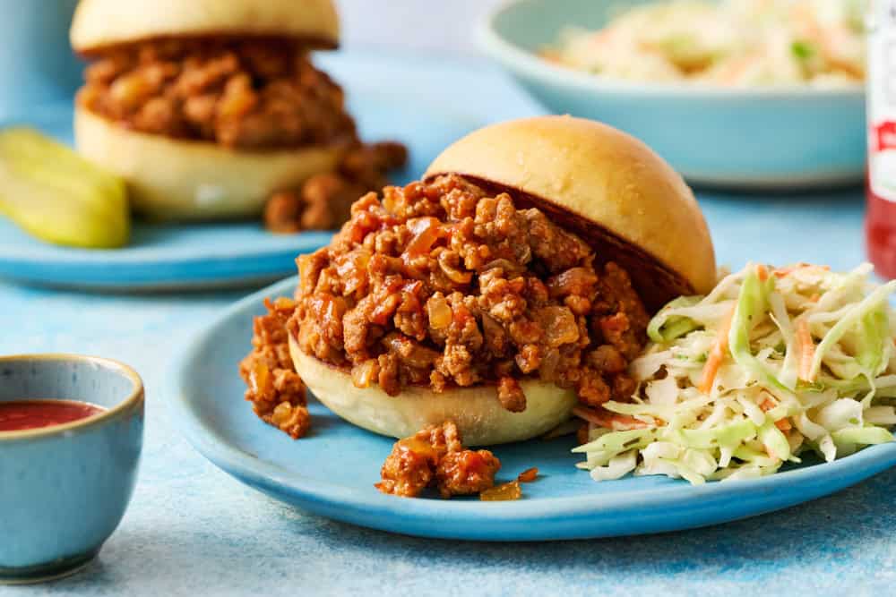 A ground chicken sloppy joes sandwich on a blue plate with another sandwich int he background.