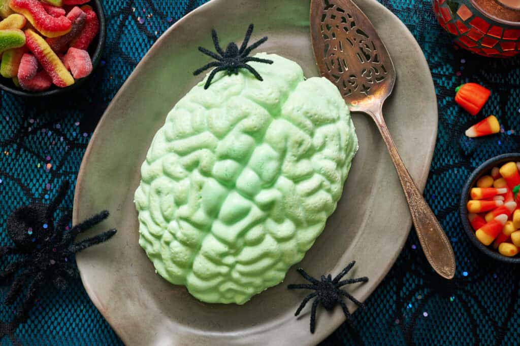 A green jello brain on a grey platter with fake spiders and a spider web tablecloth.