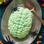 A green jello brain on a grey platter with fake spiders and a spider web tablecloth.