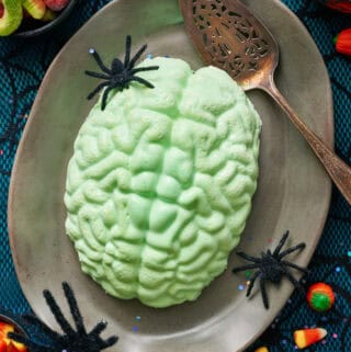 A green jello brain on a grey platter with fake spiders and a spider web tablecloth.