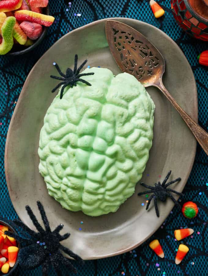 A green jello brain on a grey platter with fake spiders and a spider web tablecloth.