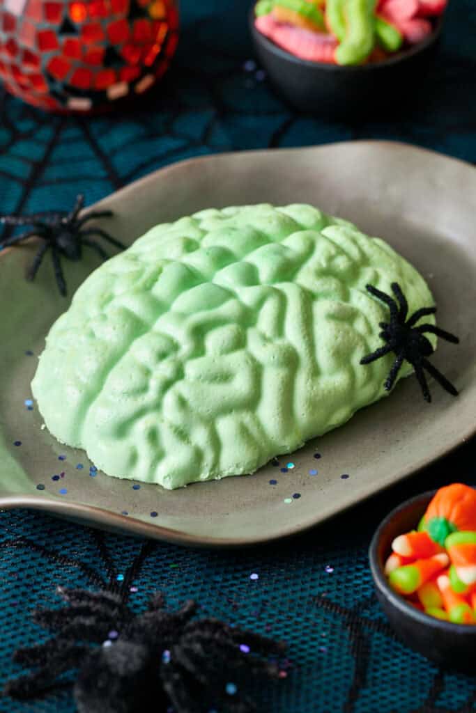 A green jello brain on a grey platter with fake spiders and a spider web tablecloth.