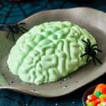 A green jello brain on a grey platter with fake spiders and a spider web tablecloth.