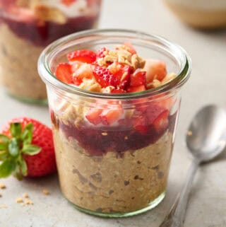 a glass jar filled with overnight oats, jelly, yogurt, chopped fruit and peanuts.