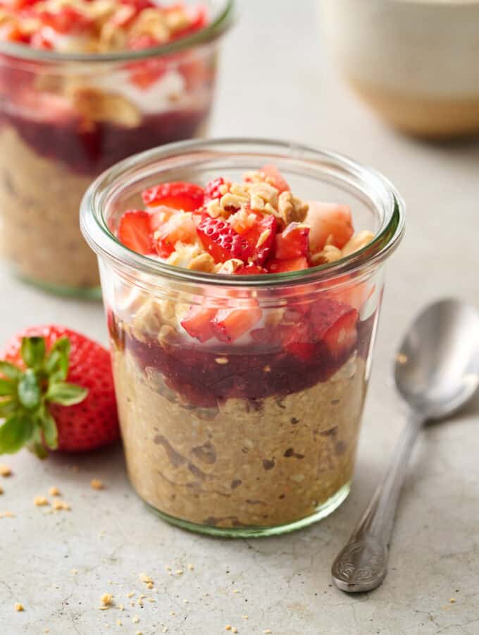 a glass jar filled with overnight oats, jelly, yogurt, chopped fruit and peanuts.