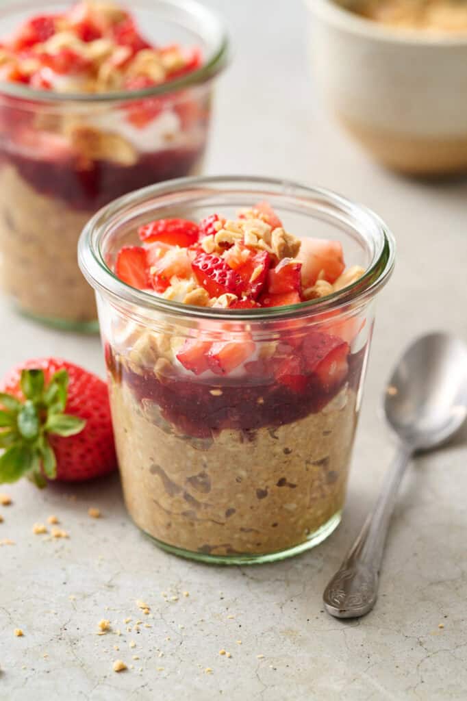 a glass jar filled with overnight oats, jelly, yogurt, chopped fruit and peanuts.