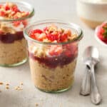 a glass jar filled with overnight oats, jelly, yogurt, chopped fruit and peanuts.