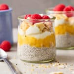 a glass jar with pineapple chia seed pudding topped with coconut and raspberries and greek yogurt