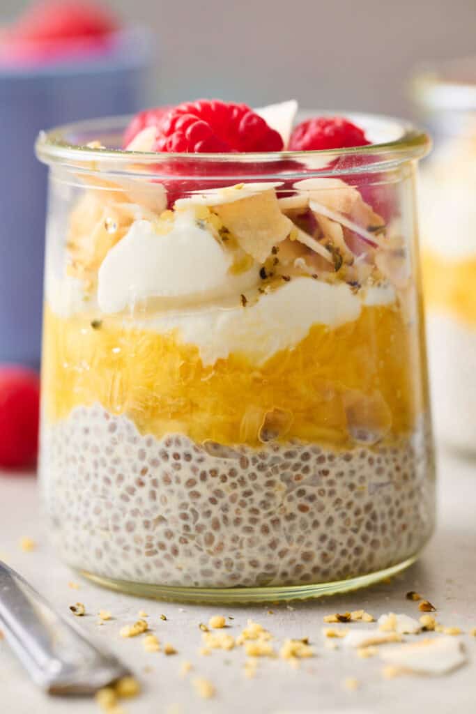 a glass jar with pineapple chia seed pudding topped with coconut and raspberries