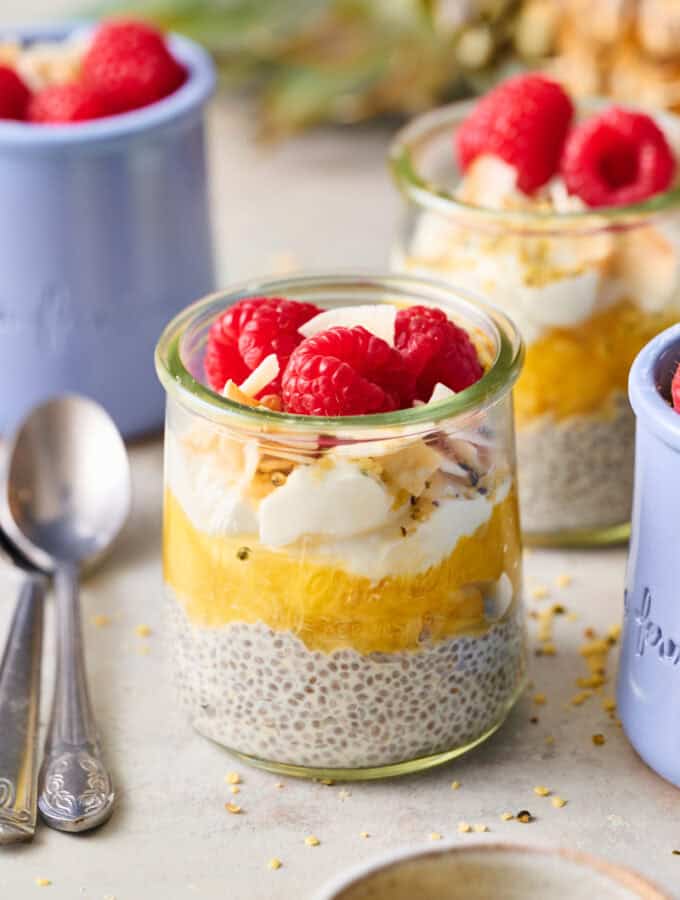 a glass jar with pineapple chia seed pudding topped with coconut and raspberries