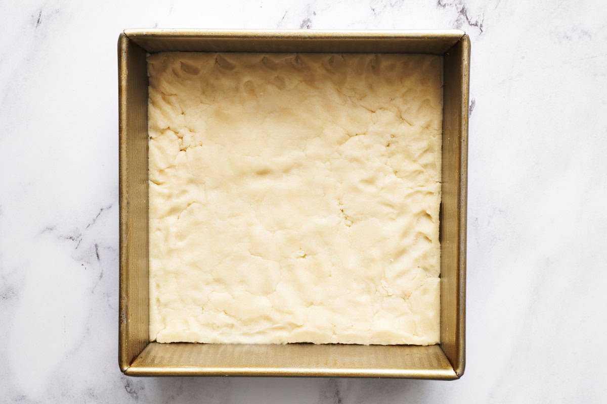 shortbread crust before it's baked in an 8 inch square metal pan