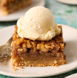 Bourbon pecan pie bar on a plate topped with ice cream and a fork on the side.