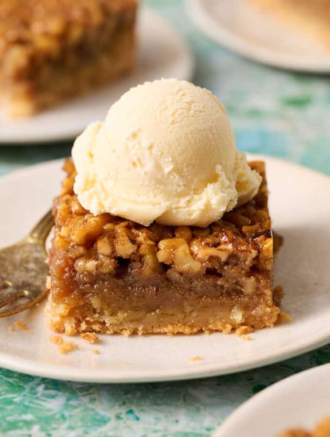 Bourbon pecan pie bar on a plate topped with ice cream and a fork on the side.