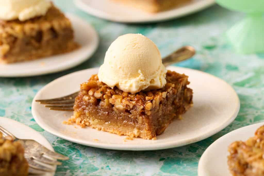 Bourbon pecan pie bar on a plate topped with ice cream and a fork on the side.