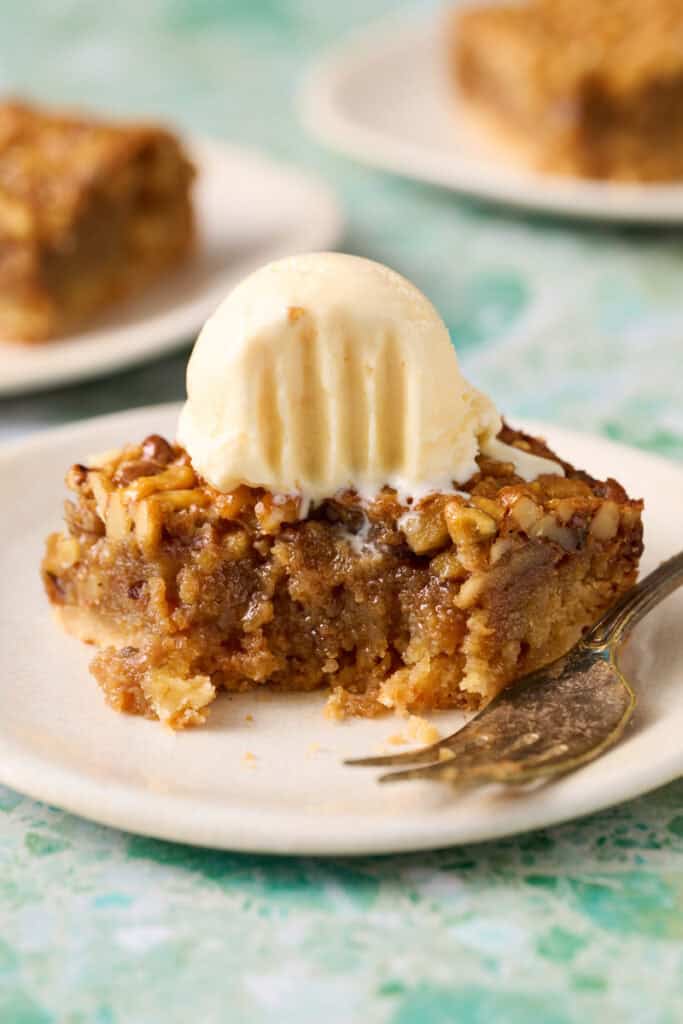 Bourbon pecan pie bar on a plate topped with ice cream and a bite taken out.