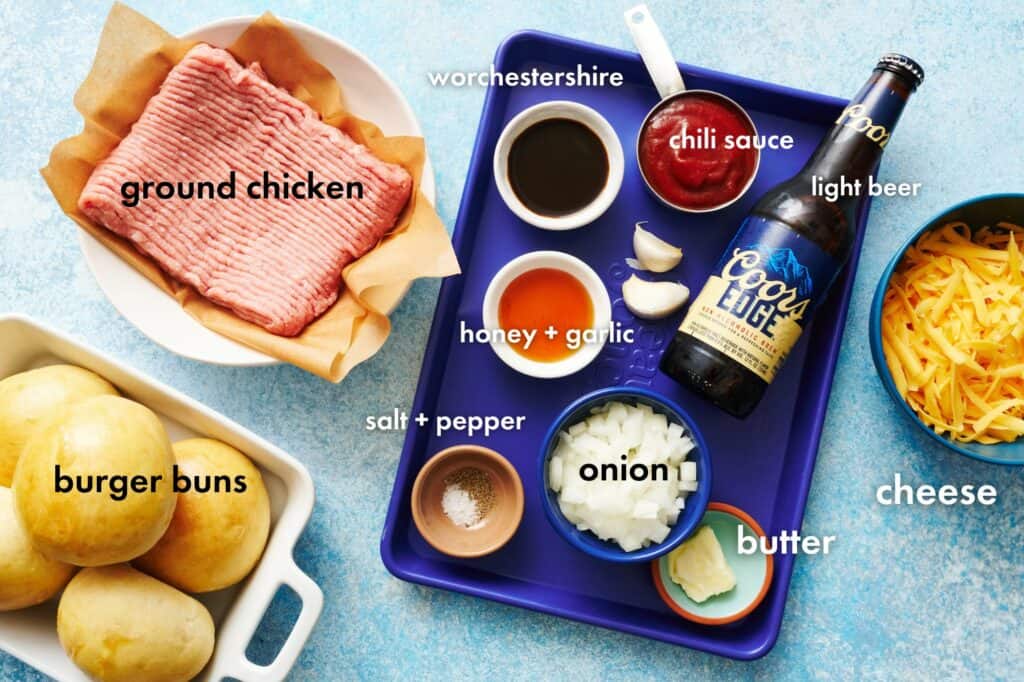 ingredients for ground chicken sloppy joes on a sheet pan including chili sauce, beer, onion, honey and garlic.