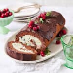 A yule log ice cream cake on a white background with a slice made and plates on the side with forks