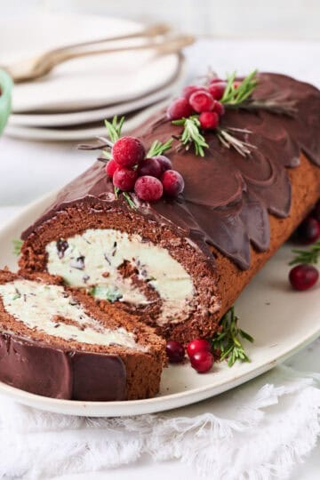 A yule log ice cream cake on a white background with a slice made and plates on the side with forks