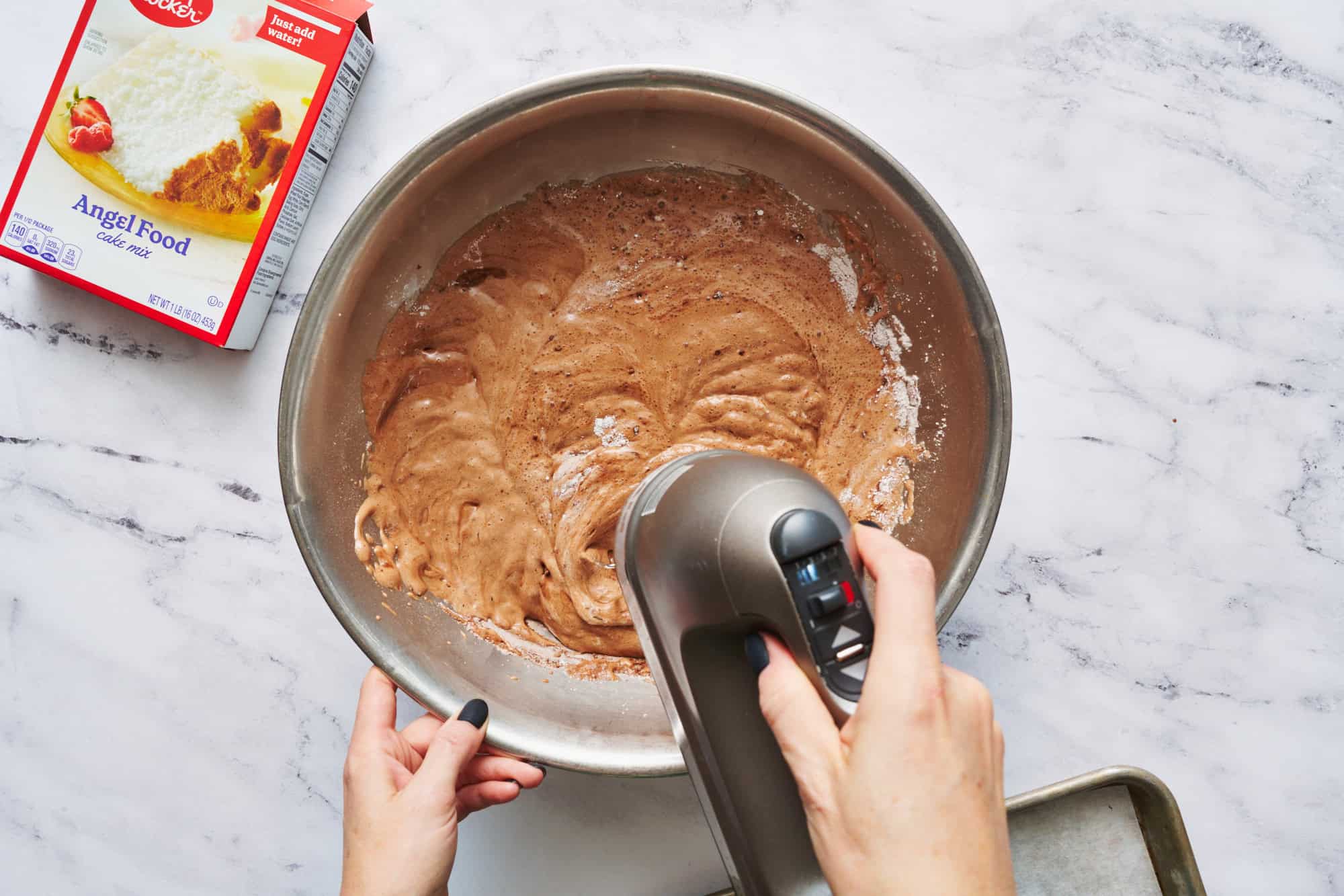 mixing up the batter of the angel food cake mix and cocoa powder and water with a hand mixer