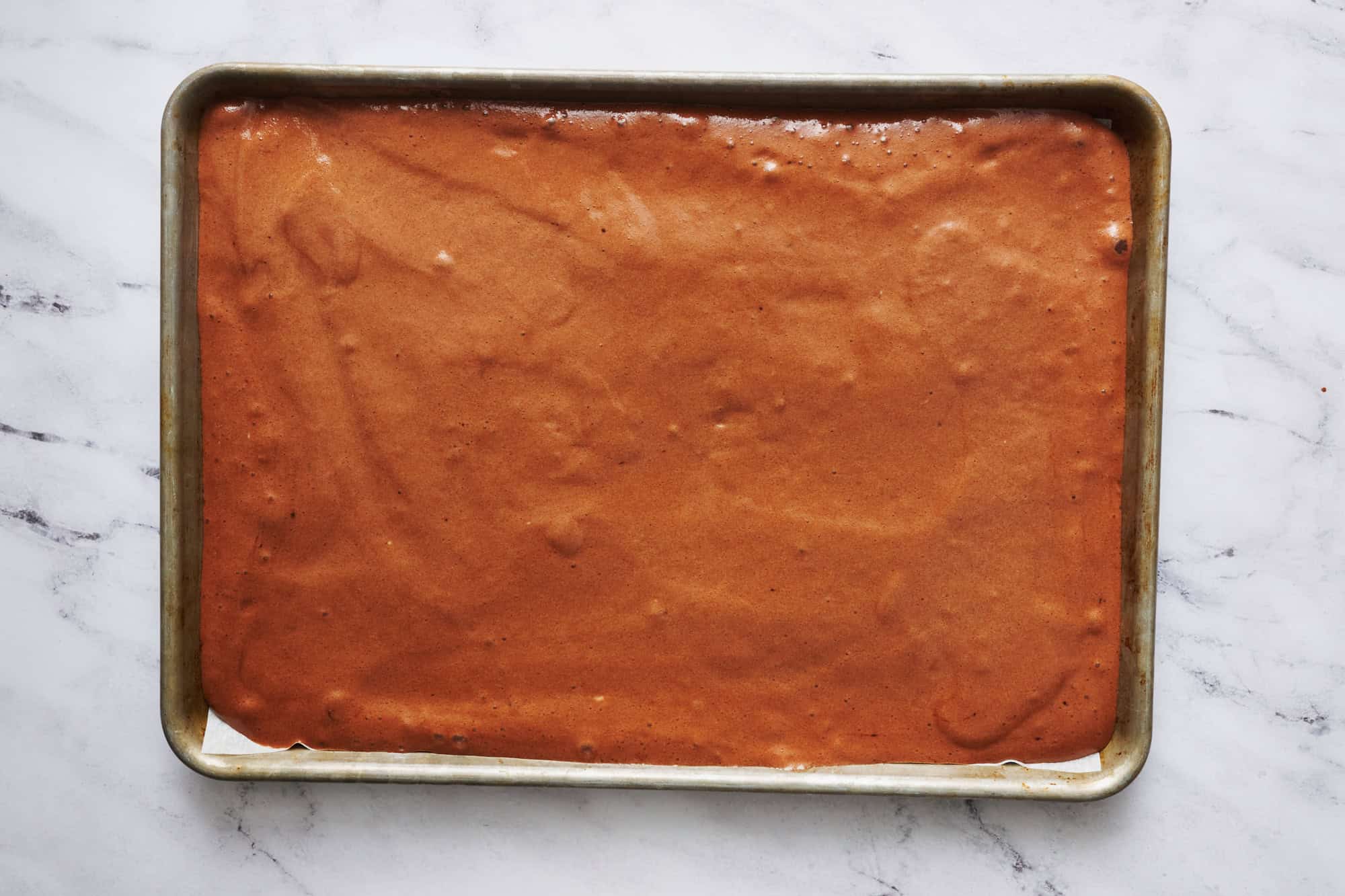 angel food cake mix with water and cocoa powder mixed and spread into a half sheet baking pan ready to bake