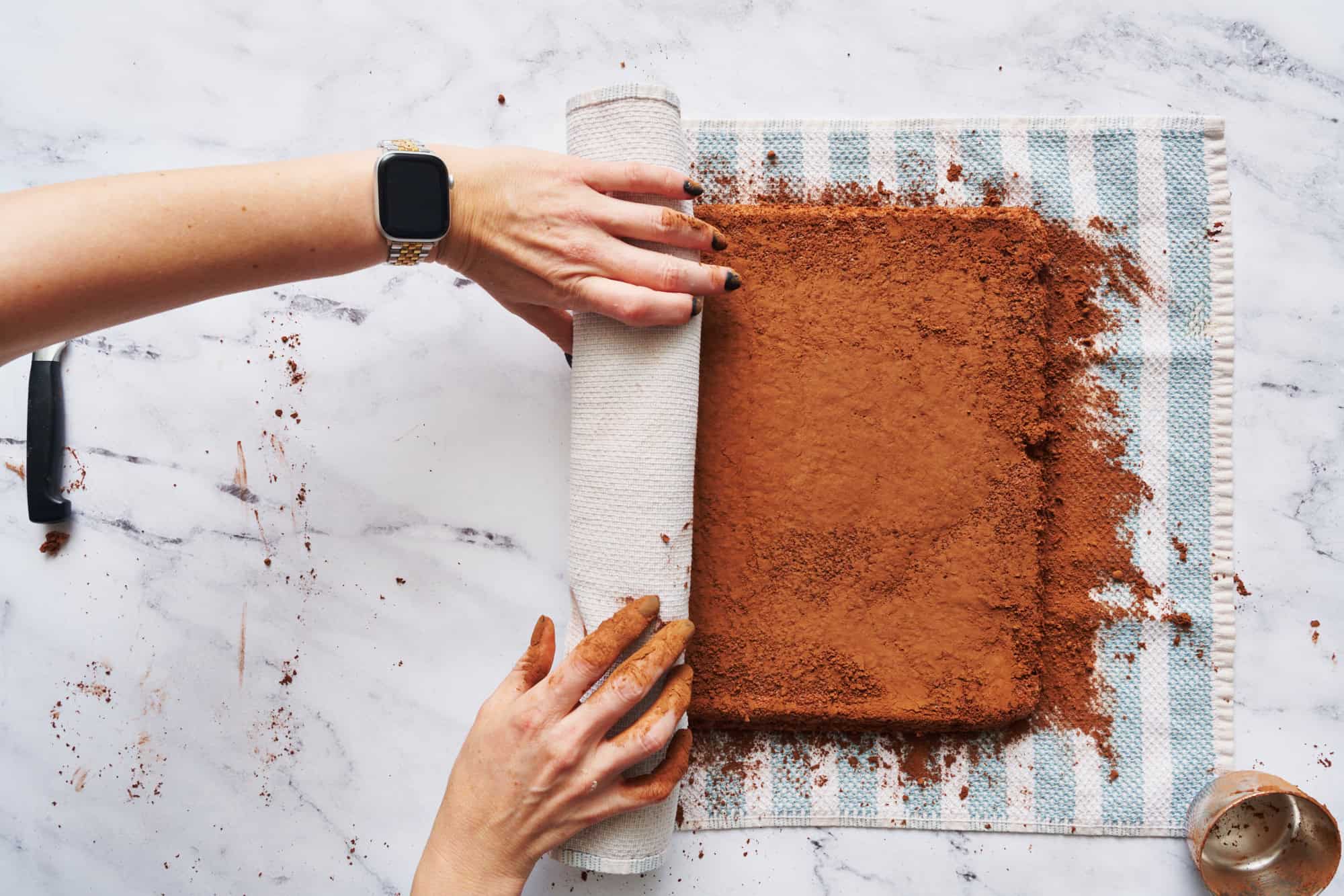 rolling up the cake after it's baked and placed on a kitchen towel with extra cocoa powder to prevent sticking