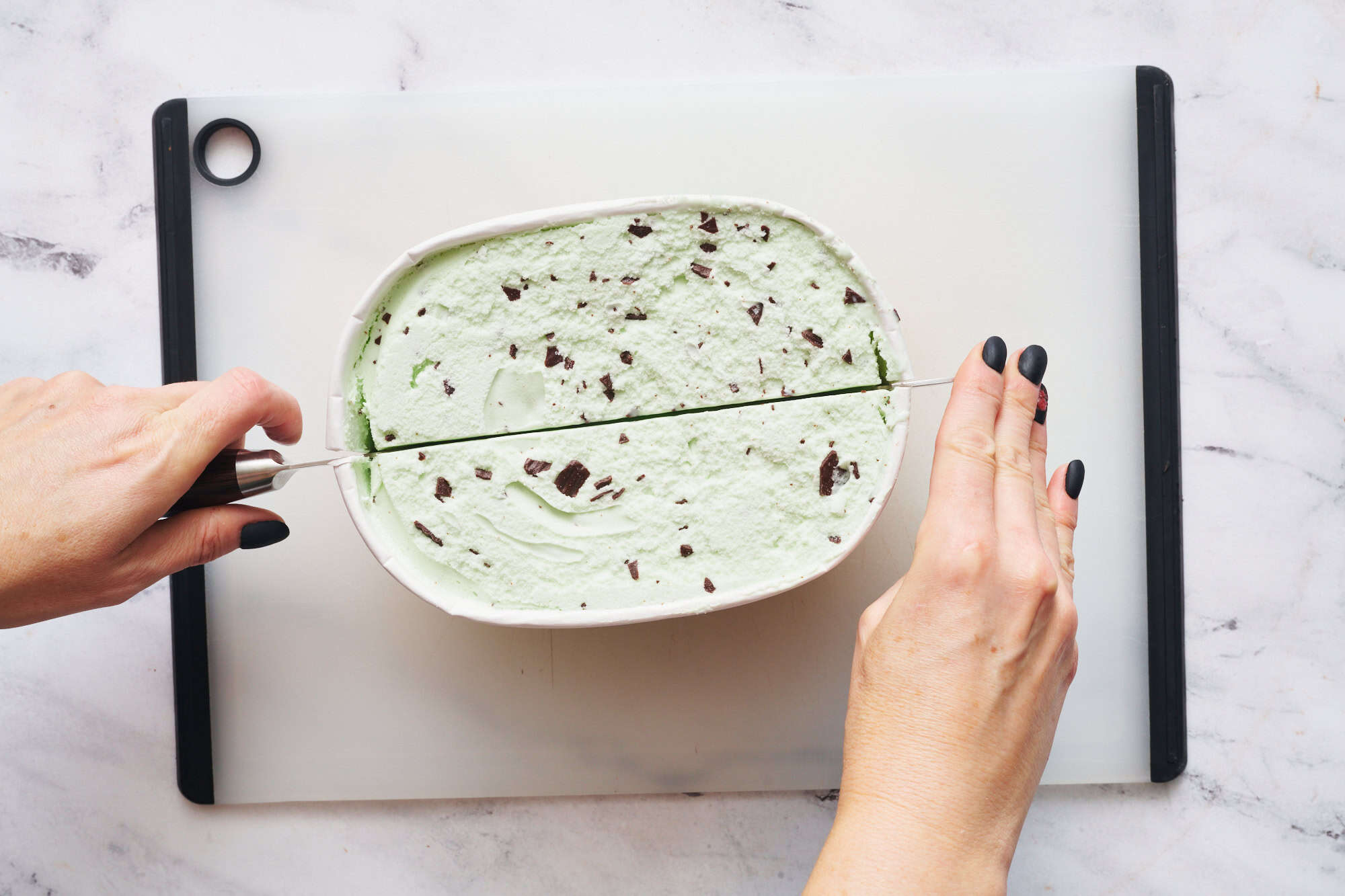 slicing a container of ice cream in half to make slices for placing in the roll cake