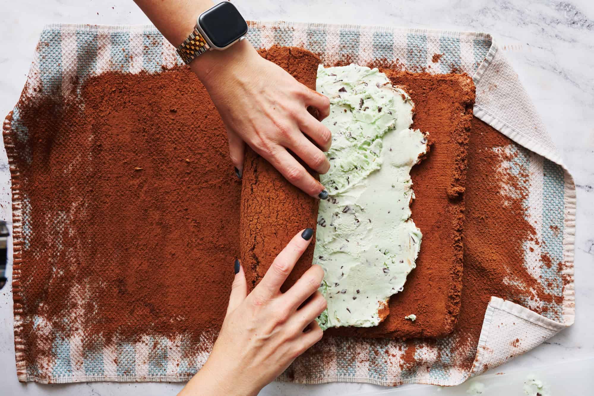 rolling up the ice cream yule log cake with lots of cocoa powder dusted on a kitchen towel