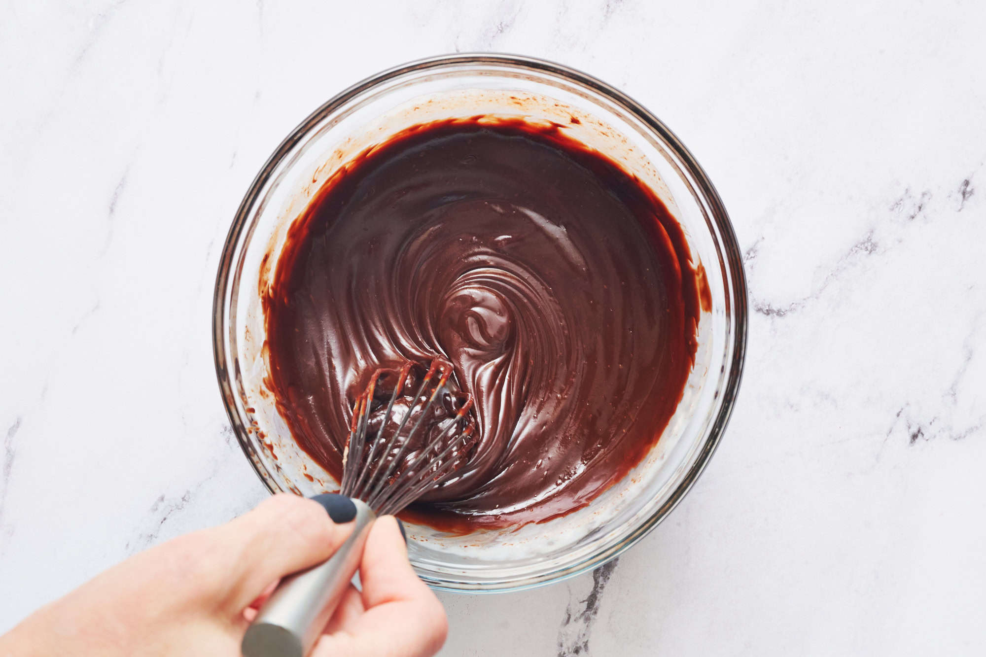 whisking a bowl of chocolate ganache to show it's smooth and melty