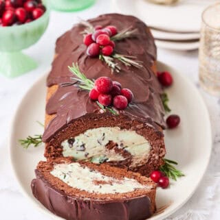 A yule log ice cream cake on a white background with a slice made and plates on the side with forks