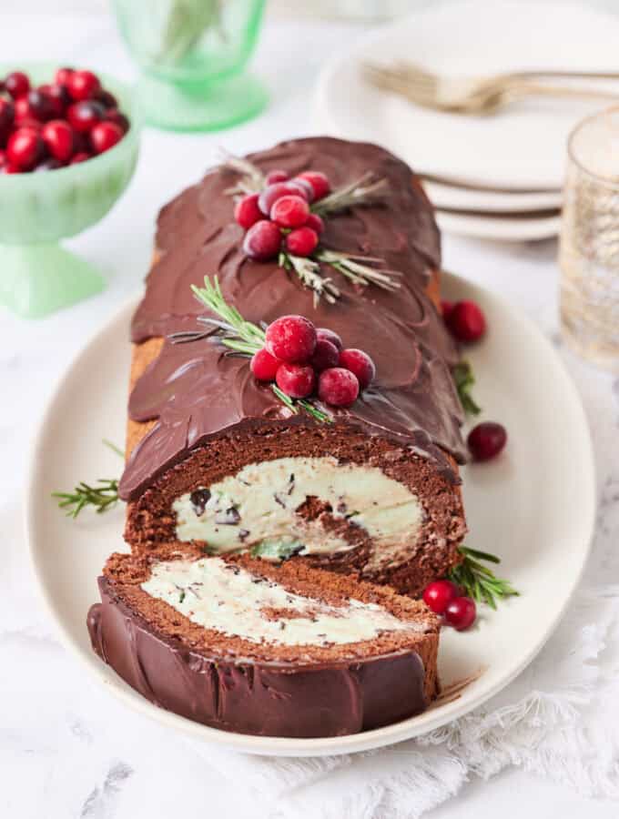 A yule log ice cream cake on a white background with a slice made and plates on the side with forks