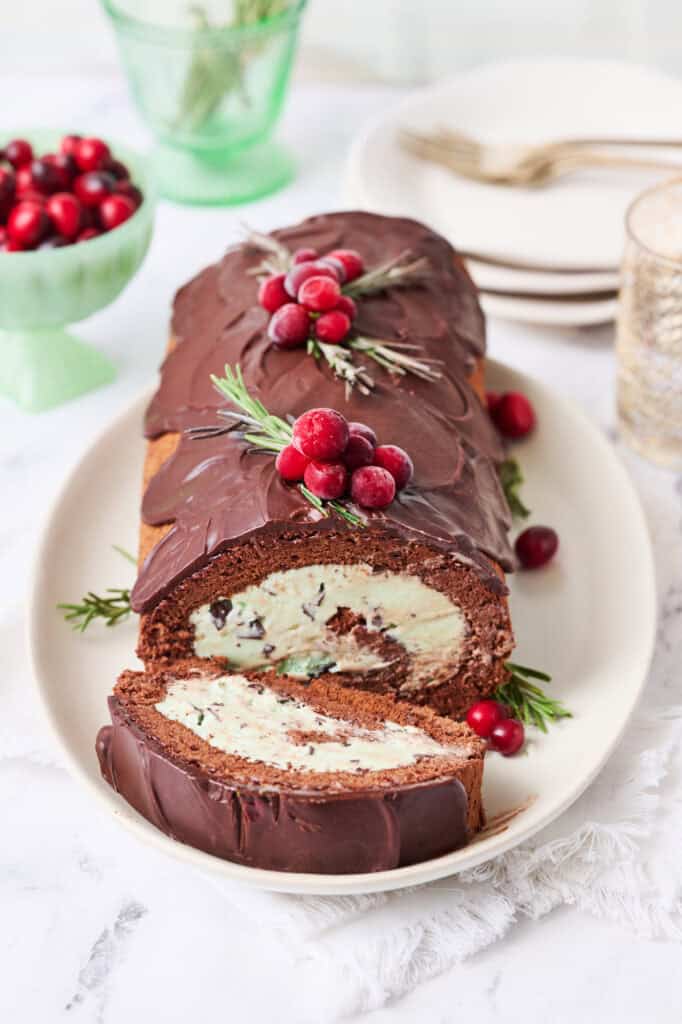 A yule log ice cream cake on a white background with a slice made and plates on the side with forks